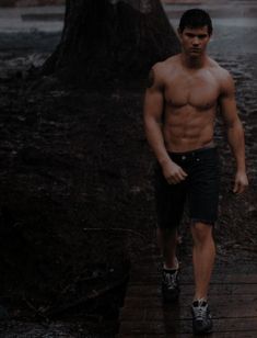 a shirtless man walking on a wooden walkway in the rain with no shirt on