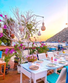 an outdoor dining area with tables, chairs and flowers on the table in front of water