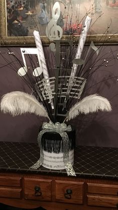 an arrangement of musical notes and feathers in a vase on a table next to a painting