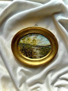 an oval painting on white fabric with gold frame