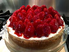 a cheesecake with strawberries on top is sitting on a glass platter next to the stove