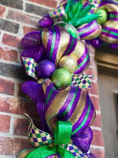 a purple and green christmas wreath hanging on the side of a brick building