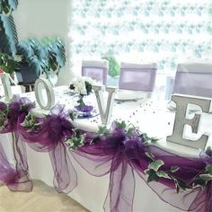 the table is decorated with purple and white flowers, greenery, and letters that spell love