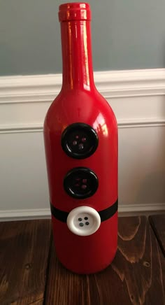 a red bottle with buttons on it sitting on top of a wooden floor next to a wall