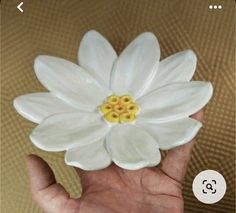 a hand holding a white ceramic flower with yellow stamens on it's center