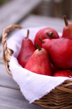 a basket filled with red pears sitting on top of a wooden table