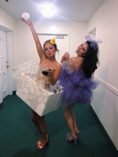 two women dressed in costumes are holding wine glasses and soap bubbles as they pose for the camera