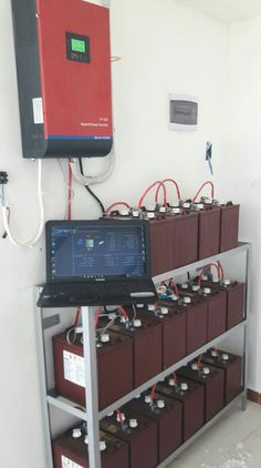 a laptop computer sitting on top of a metal shelf filled with lots of red and black batteries