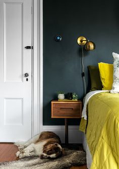 a dog laying on the floor in front of a bed with yellow sheets and pillows