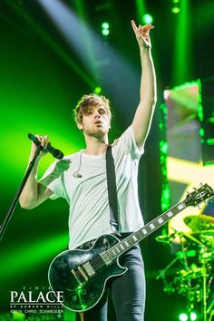 a man with a guitar on stage waving to the crowd while holding his hand up