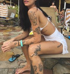 a woman with tattoos on her body sitting on a bench in front of some chairs