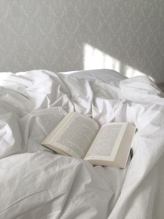 an open book laying on top of a white bed