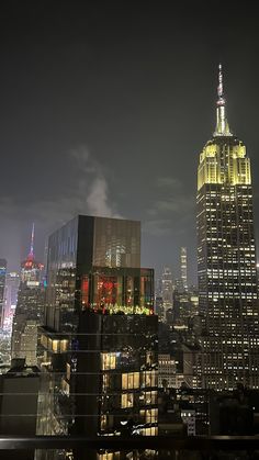 the empire building is lit up at night in new york city, with other skyscrapers visible