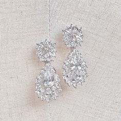 two pairs of diamond earrings sitting on top of a white cloth