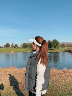 a woman standing on top of a grass covered field next to a lake with a kite flying in the sky