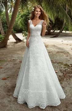 a woman in a white wedding dress standing on the beach with palm trees behind her