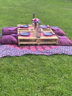 a picnic table set up in the grass with purple pillows and place settings on it