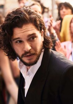 a man with curly hair and beard wearing a black suit in front of a crowd