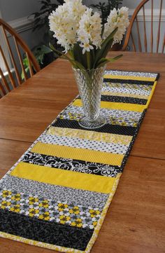 a vase filled with white flowers sitting on top of a wooden table next to a yellow and black runner