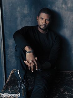 a man sitting on top of a wooden table next to a blue wall and wearing black pants