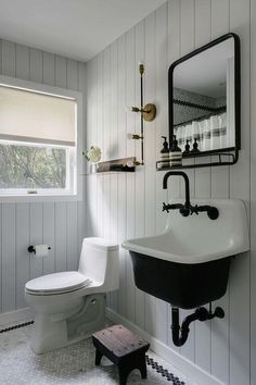 a white toilet sitting next to a black sink in a bathroom under a large mirror