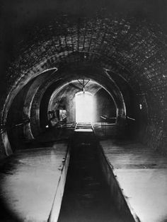 an old black and white photo of a dark tunnel with light coming in from the end