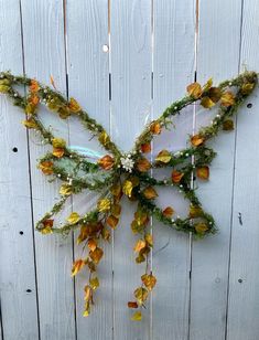 a butterfly made out of branches and flowers on a wooden fence with white pickets