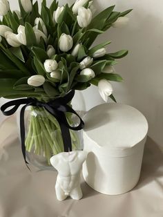 a vase filled with white tulips next to a small elephant figurine