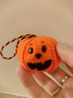 a hand holding an orange felt pumpkin with a spider on it's head and eyes