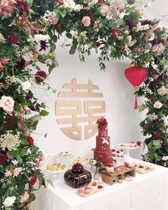 a table topped with cakes and desserts next to a flower covered wall behind it