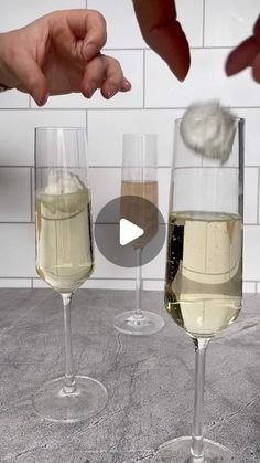 two champagne flutes being filled with white wine by someone reaching for the one in front