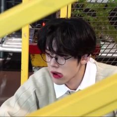 a young man wearing glasses sitting in front of a yellow fence