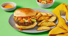 a hamburger and some potato wedges on a plate with a bowl of dipping sauce