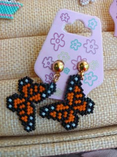 two small black and orange earrings on a piece of fabric next to a pink bag