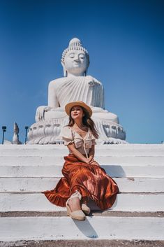 a woman sitting on steps in front of a large buddha statue