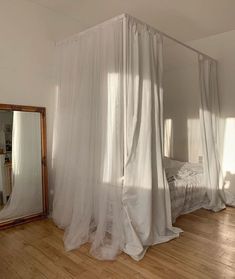 a white canopy bed sitting on top of a hard wood floor next to a mirror