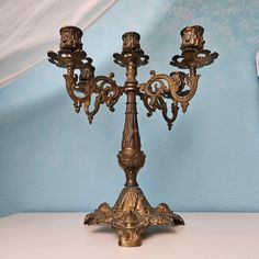 an ornate brass candelabra with three candles on it's sides against a blue background