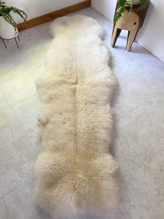 a white sheepskin rug on the floor next to a chair and potted plant