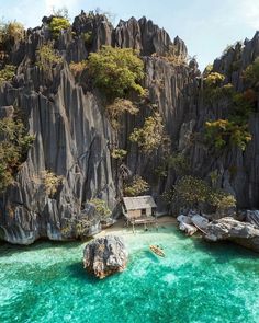 there are two people in the water near some rocks and trees on the shore with a hut