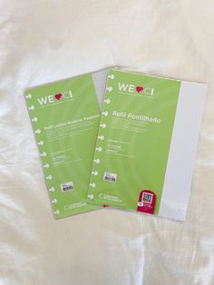 two green notebooks sitting next to each other on a white sheet covered bedding