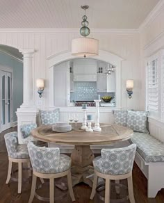 a dining room table with four chairs and a bench in front of an archway leading to the kitchen