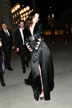 a woman in a black dress is walking down the street with other people behind her