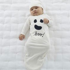 a baby laying on top of a bed wearing a white outfit with a smiley face