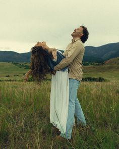 a man and woman are standing in the grass with their arms around each other as they look up into the sky