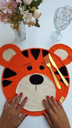 a woman is holding a crocheted placemat with a tiger face on it