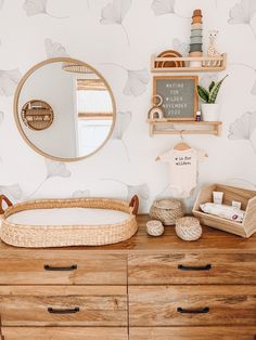 a wooden dresser topped with a baby's crib next to a round mirror