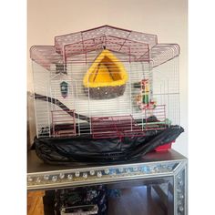 a caged bird sits on top of a table in front of a mirror with a yellow cone hanging from it's roof