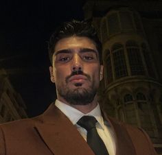 a man wearing a suit and tie in front of a building at night with his eyes closed