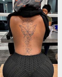 a woman with a butterfly tattoo on her back sitting at a table in front of a counter