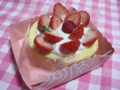 there is a cake with strawberries on it sitting on a pink and white checkered tablecloth